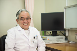 白衣を着た医療職員が医務室で笑顔でカメラに向かっている
